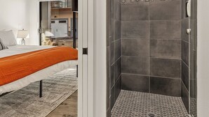 A modern bathroom with a shower, a bed with an orange bedspread, and a ceiling fan.