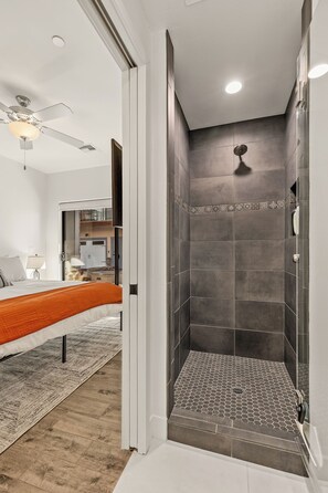 A modern bathroom with a shower, a bed with an orange bedspread, and a ceiling fan. - Downtown - 3BR/3.5BA - 5 Patios - Mnt. Views - 7 Guests (Flagstaff)