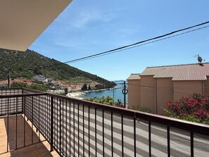 A balcony with a view of a coastal area, including a body of water and a hilly landscape. - Apartments Benzia (Marina)