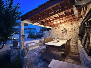 An outdoor patio with stone walls, wooden furniture, and a stone table. - Apartments Benzia (Marina)