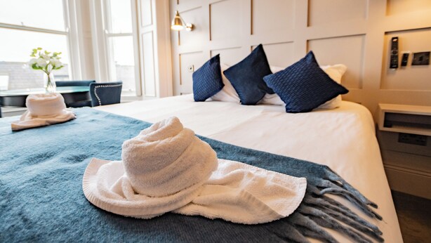 A hotel room with a neatly made bed, a blue towel, and a white hat on the bed.
