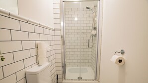 A small bathroom with a toilet, a shower stall, and a toilet paper holder.
