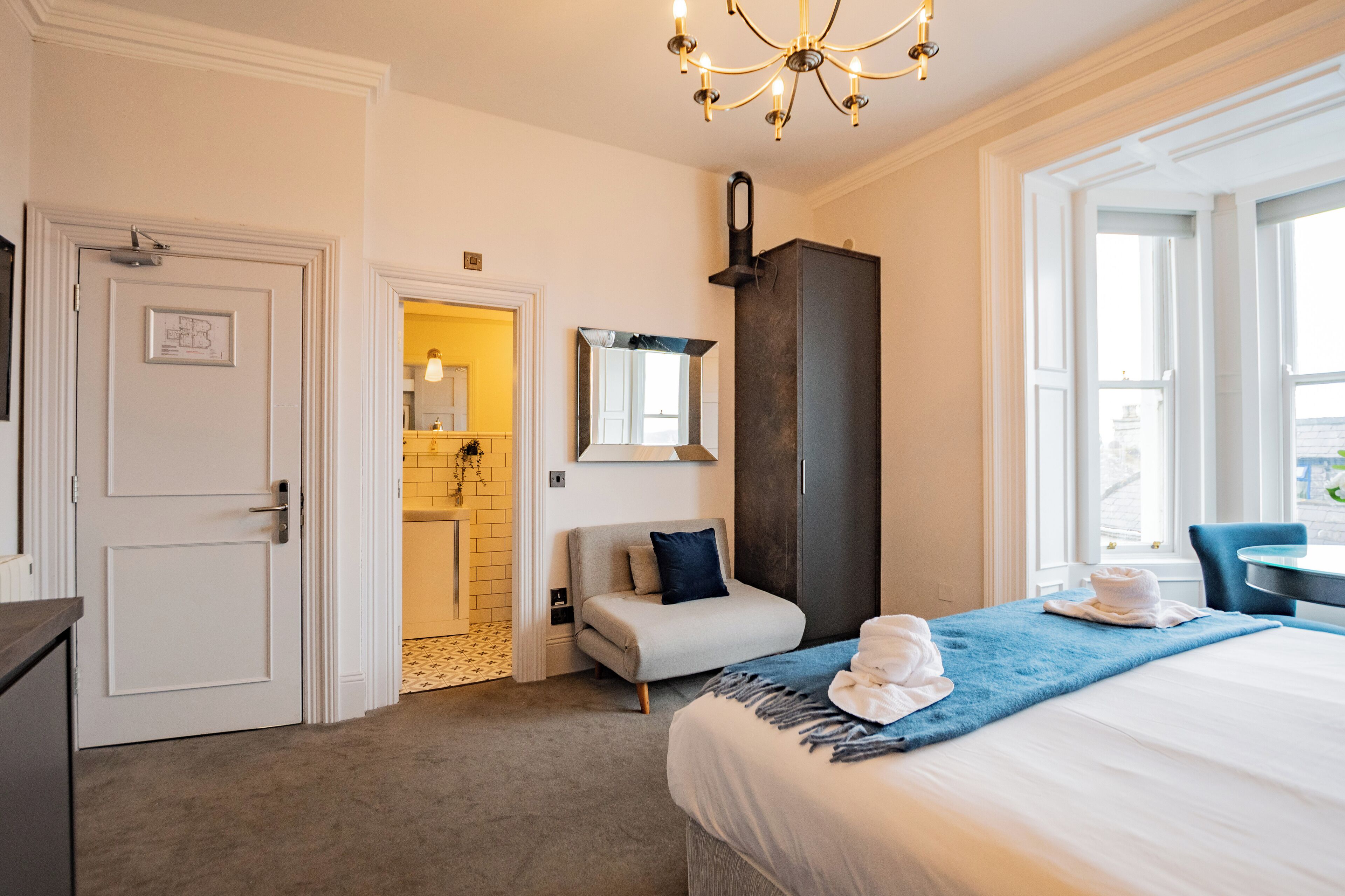 Una habitación de hotel con cama, escritorio, silla, espejo, armario y puerta.