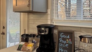 Una cocina con cafetera, un cartel que dice 'Good Days Start Here' y una ventana con persianas.