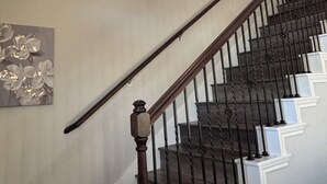 Una escalera con barandilla de madera y balaustres negros, que conduce a un rellano con una lámpara.