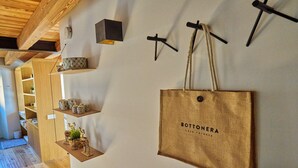 En væg med en stor trætaske mærket "BOTTONERA Casa Vacanza", hylder med dekorative genstande og et træloft.