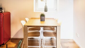 Et spiseområde med et træbord, stole, en hængende lampe, et vindue med en plante og et rødt skab.