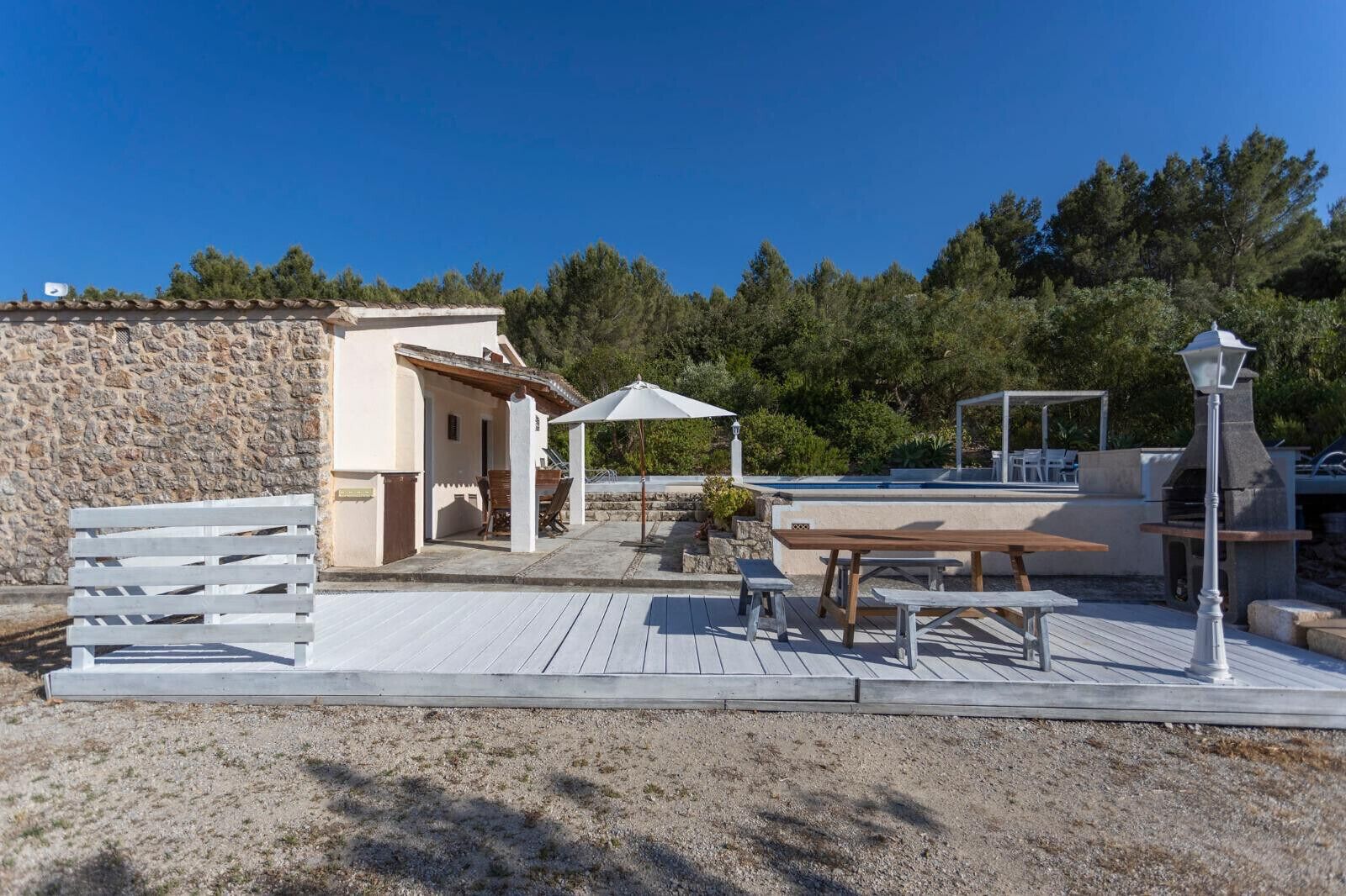 A wooden deck with a table and benches, a stone wall, and a pool area with a pergola.