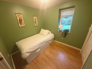 A small bedroom with a single bed, green walls, and a window with blinds. - ocean view, backyard w/fire pit, 5 min walk to cafes/beach, dogs welcome (Tillamook)