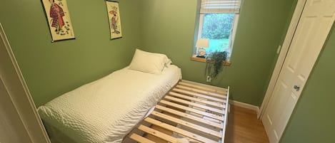 Una habitación pequeña con cama individual, cabecero de madera, paredes verdes y dos cuadros colgados.