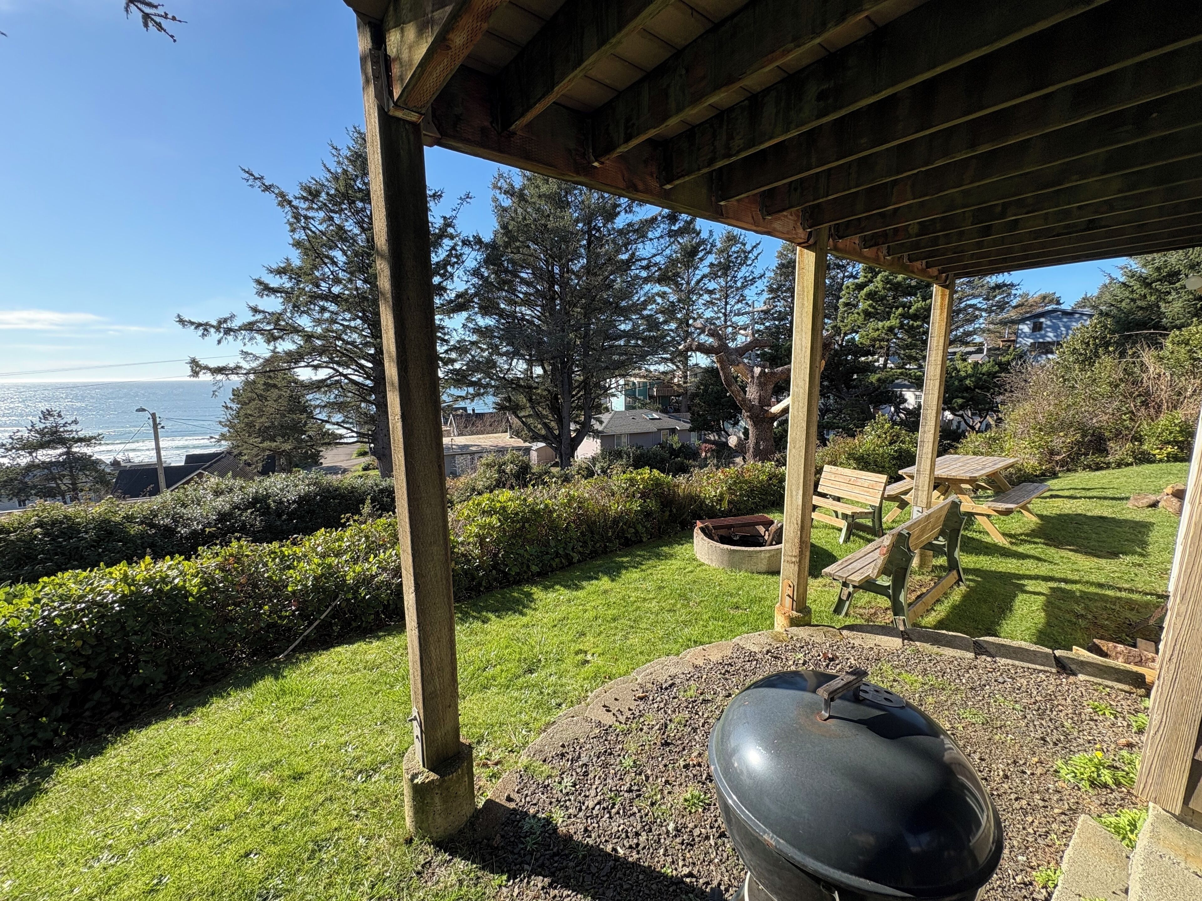A covered outdoor area with a barbecue grill, wooden benches, and a view of the ocean.
