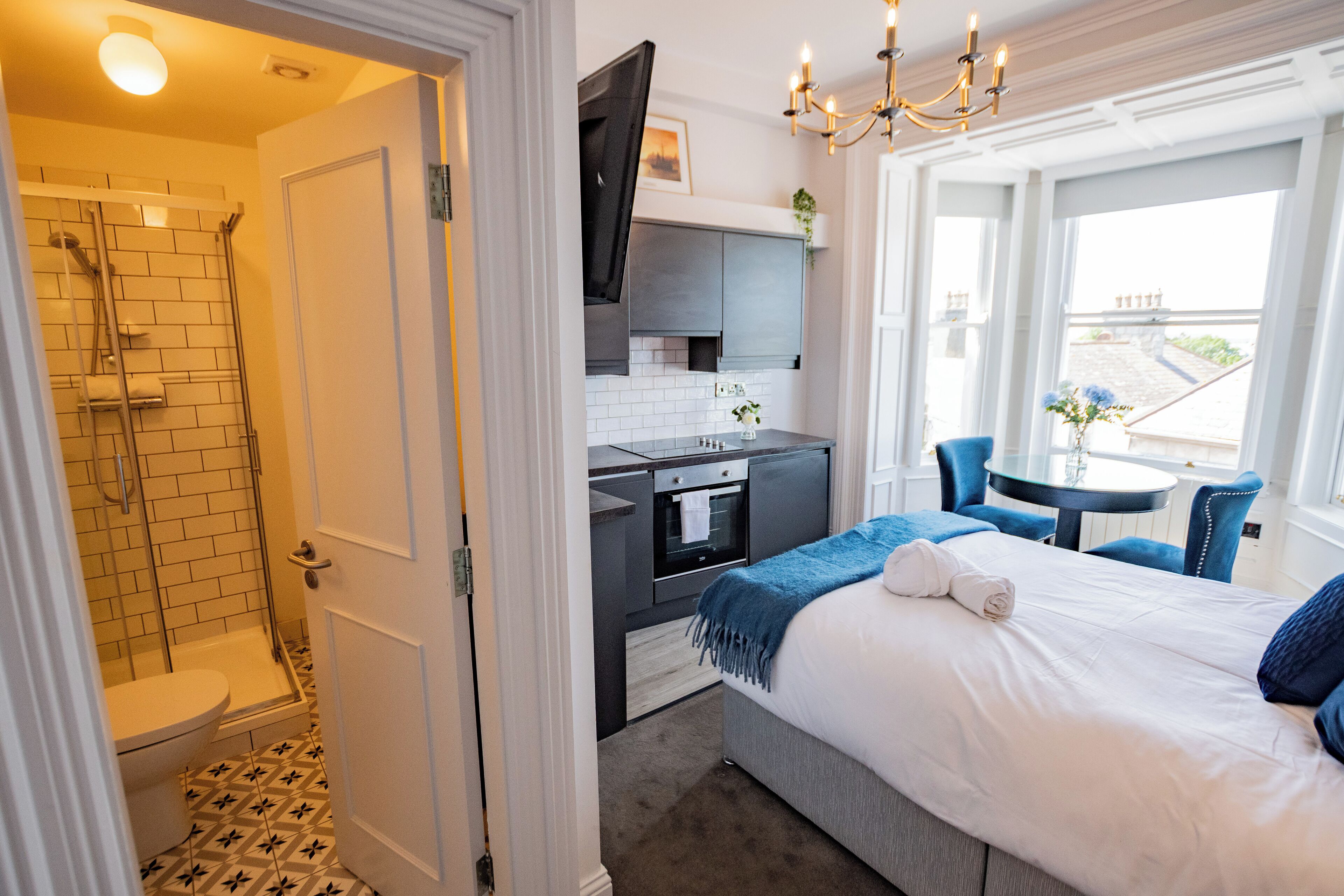 A compact hotel room with a shower, kitchenette, and a bed with a view.