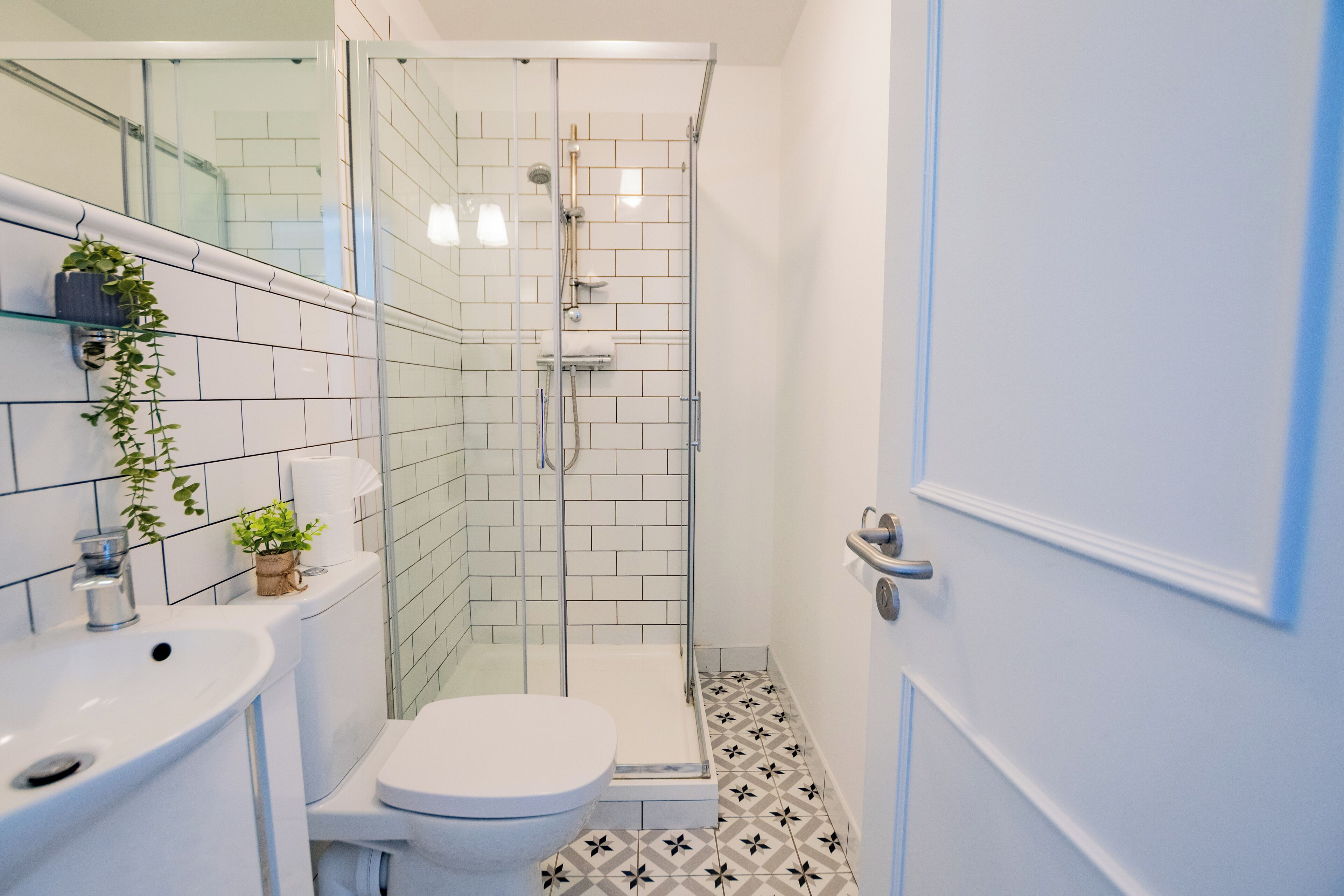 Une salle de bain avec un lavabo blanc, des toilettes et une douche fermée par des parois en verre.