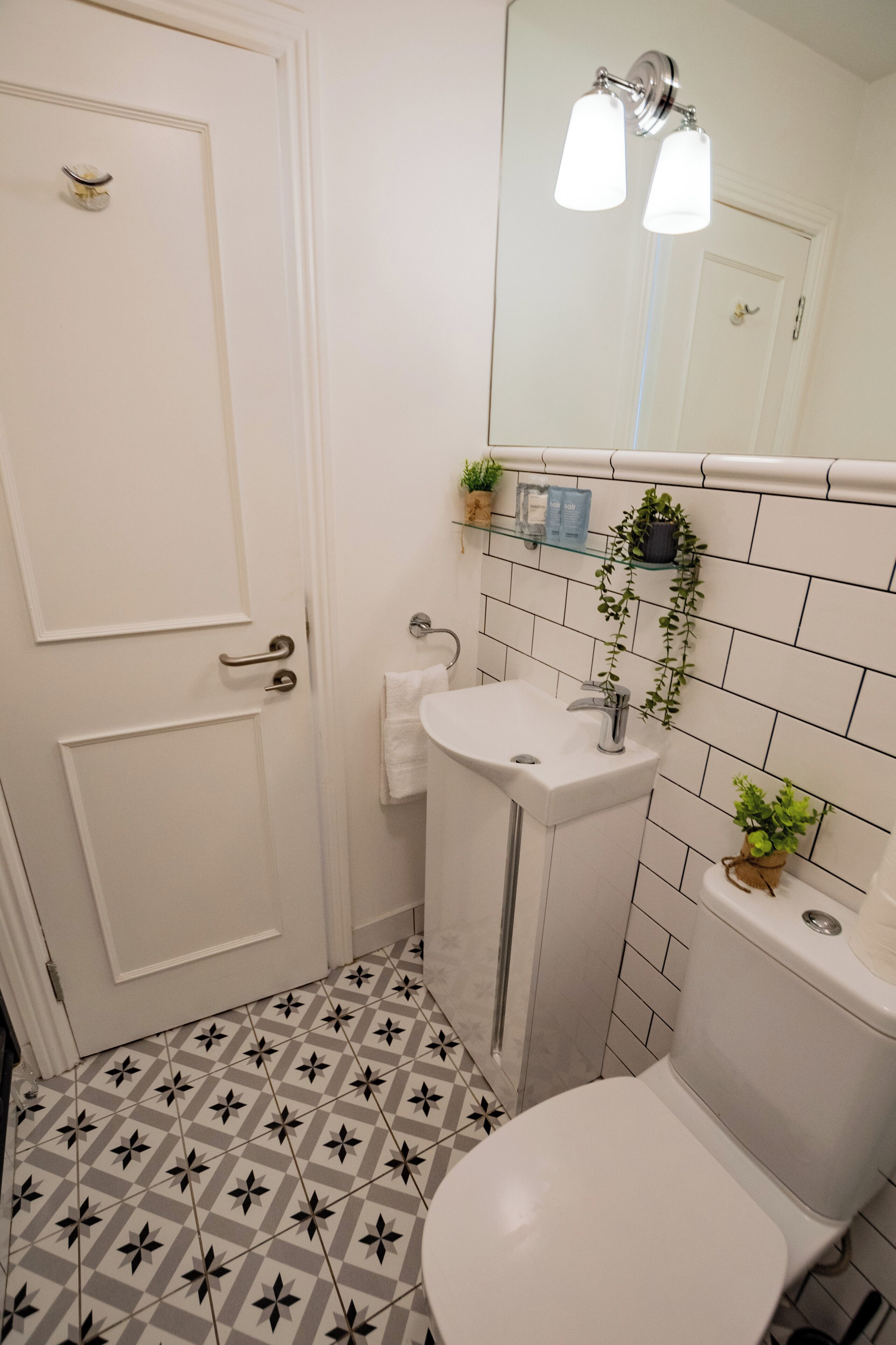 Une salle de bain avec des toilettes blanches, un lavabo surmonté d’un miroir et un carrelage décoratif.