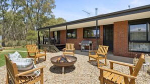Een terras buiten met houten stoelen, een vuurkorf en een barbecuehoek.