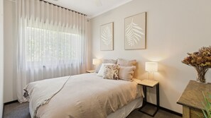 A bedroom with a bed, two bedside tables, a nightstand, a window with sheer curtains, and two wall-mounted leaf-patterned artworks. - One Mile Creek Retreat (Wangaratta)