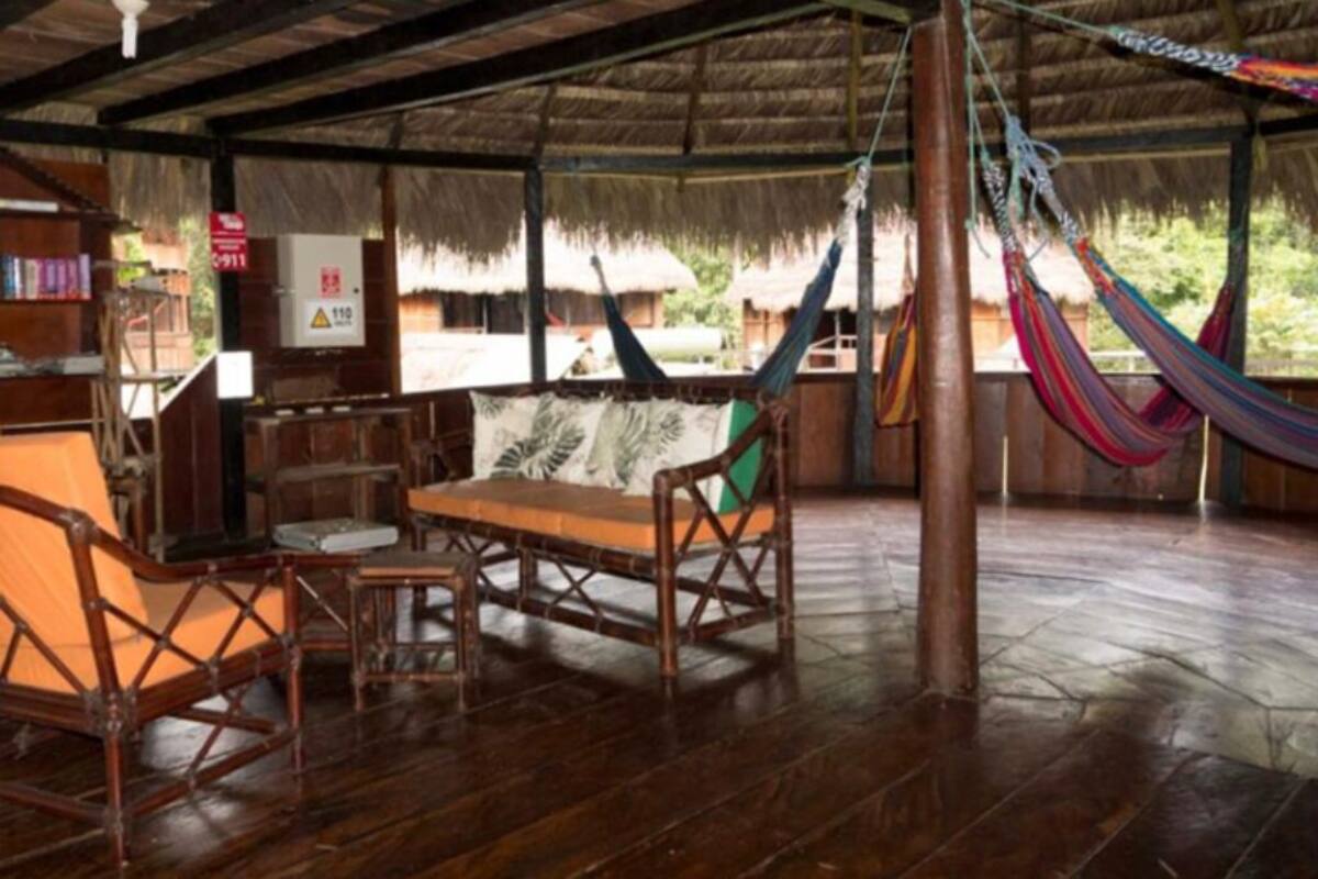 A wooden room with a thatched roof, a hammock, and a wooden table with chairs.