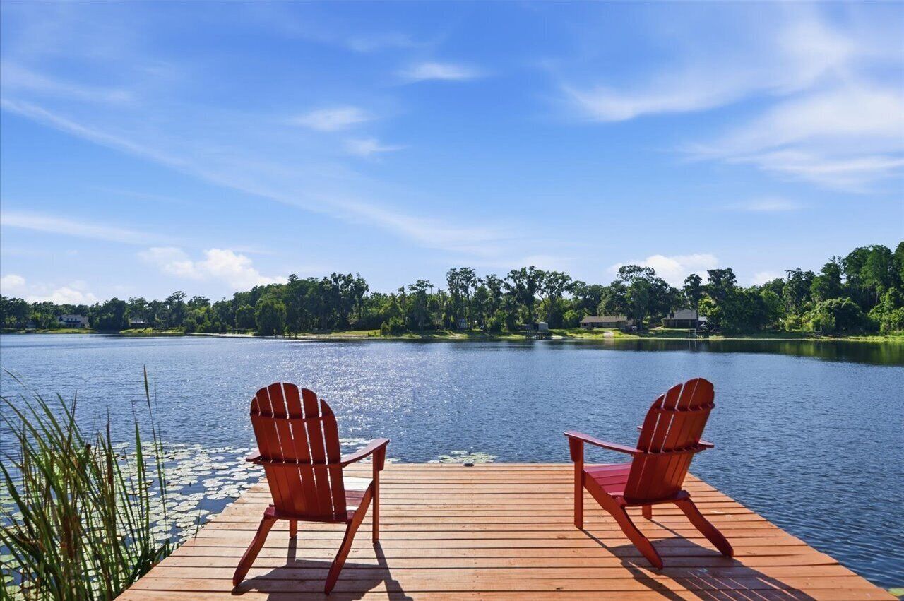 A wooden dock with two red Adirondack chairs facing a calm lake.