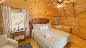 Un dormitorio de cabaña de madera con una cama, una mesita de noche, una lámpara, una silla, un armario de madera y un ventilador de techo.