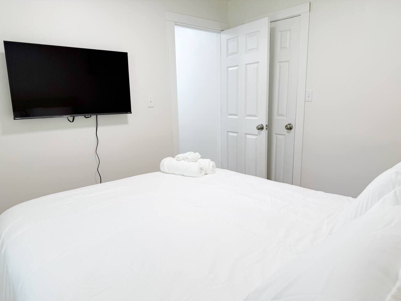 A bedroom with a bed, a flat-screen TV mounted on the wall, and a door.