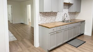 A kitchen with light grey cabinets, a wooden countertop, and a tiled backsplash. - The Homestead House (Henderson)