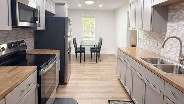 A modern kitchen with a central island, built-in appliances, and a dining area with a window. - The Homestead House (Henderson)