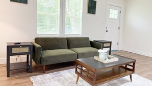 A living room with a green sofa, a wooden coffee table, and two side tables. - The Homestead House (Henderson)