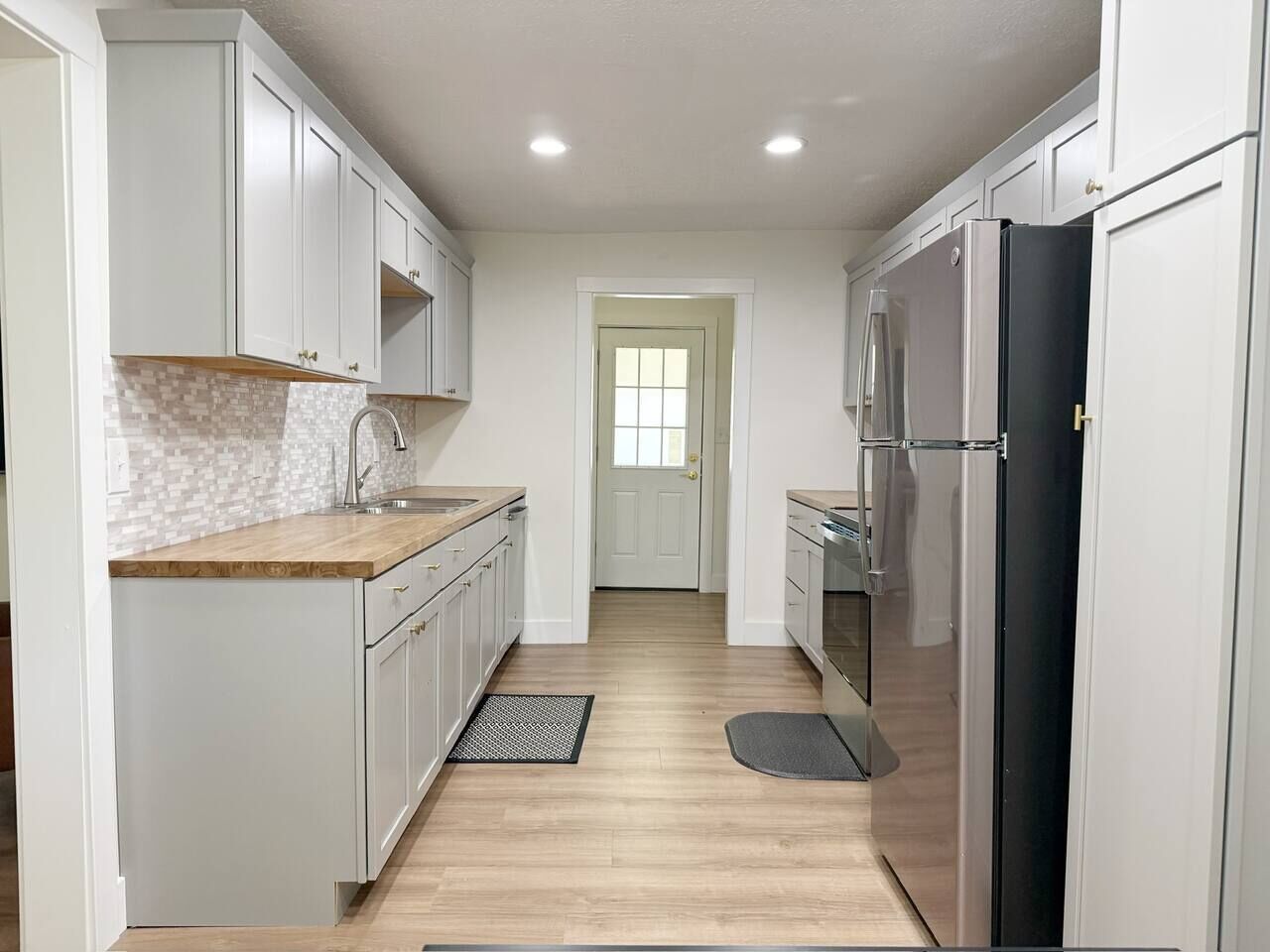 A narrow kitchen with white cabinets, a wooden countertop, and a black refrigerator.