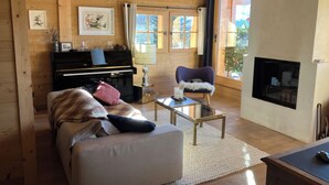 A cozy log cabin interior with a piano, a fireplace, a sofa, and a chair. - FAMILY CHALET FOR RENT (Manigod)