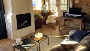 A cozy cabin interior with a fireplace, wooden walls, a desk with a computer, a comfortable chair, and a sofa. - FAMILY CHALET FOR RENT (Manigod)