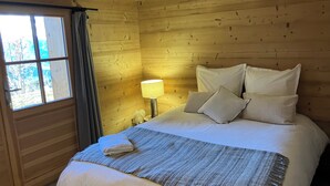 A wooden-paneled room with a bed, a window, and a nightstand with a lamp. - FAMILY CHALET FOR RENT (Manigod)