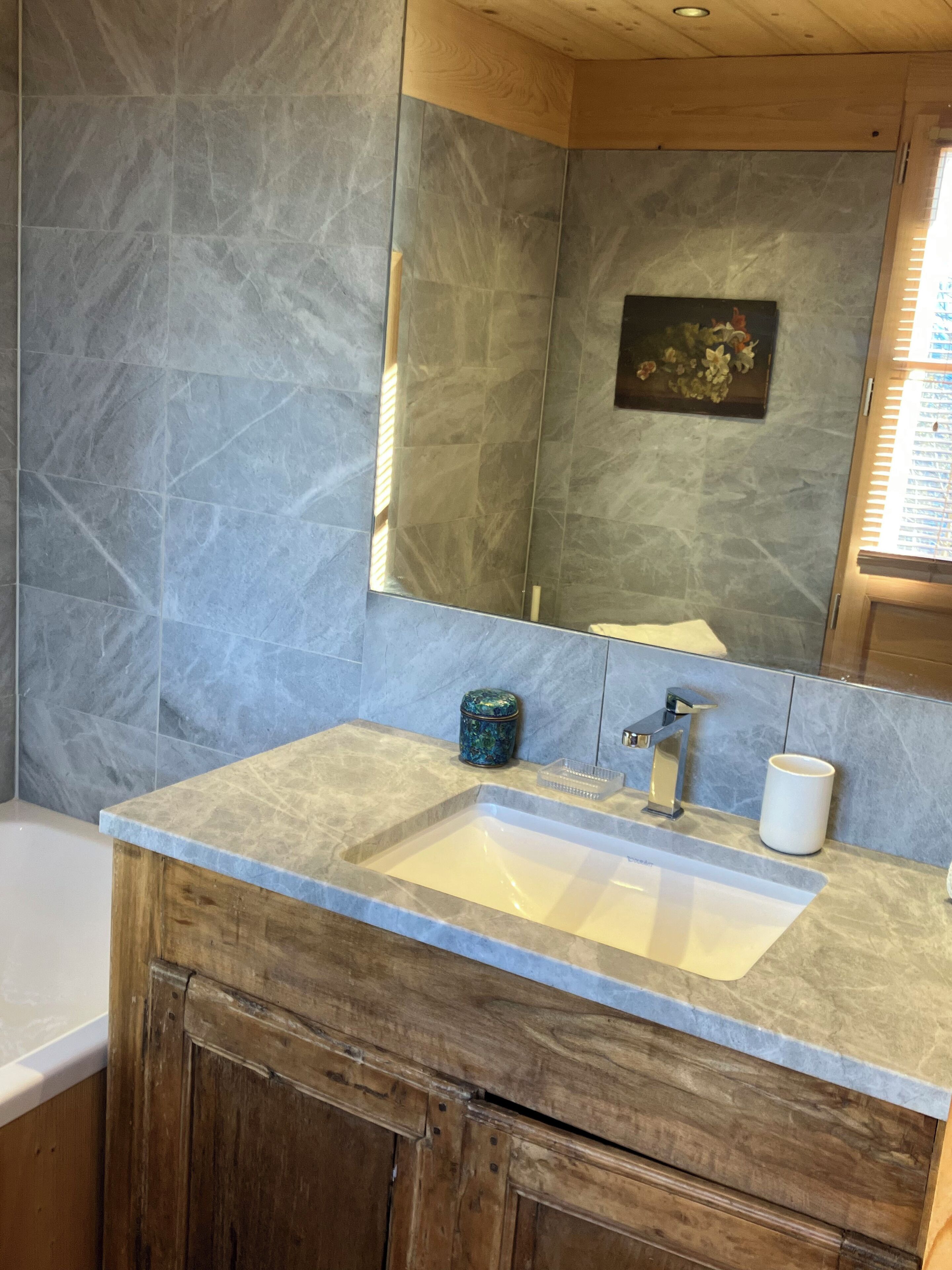A bathroom with a marble sink, wooden cabinet, and a mirror.