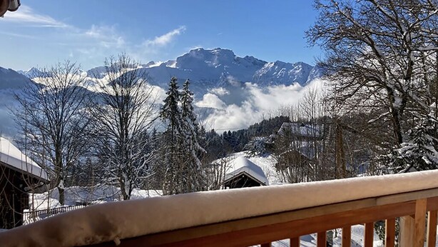 A snowy mountain landscape with a wooden balcony railing. - FAMILY CHALET FOR RENT (Manigod)