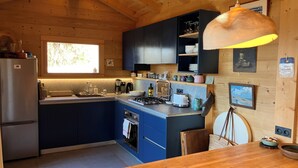 A modern kitchen with blue cabinets, a wooden dining table, and a pendant light. - FAMILY CHALET FOR RENT (Manigod)