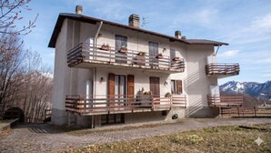 Edifici de dues plantes amb balcons, un camí de maó i un paisatge de muntanya de fons.