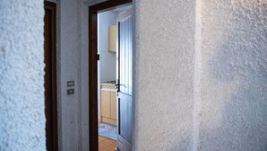 Passadís estret que condueix a una cuina amb armaris de fusta i terra de rajola.