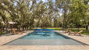 Ein rechteckiger Swimmingpool mit blauer Liegefläche, umgeben von Liegestühlen und einer Ziegelterrasse.
