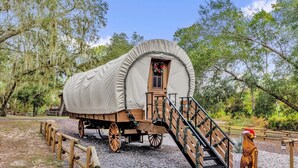 Ein beladener Wagen mit einer Holzrampe, die zu einer Tür führt, umgeben von Bäumen und Kies.