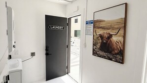 A clean, modern hallway with a sign for the laundry room, a mounted picture of a yak, and a white tiled floor. - Quiet Newly Renovated Oasis in the Heart of North Park (San Diego)