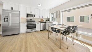 A modern kitchen with white cabinets, stainless steel appliances, and a dining area with a table and chairs. - Quiet Newly Renovated Oasis in the Heart of North Park (San Diego)