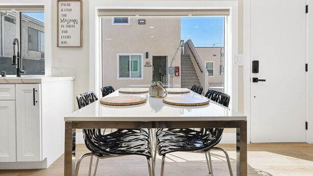 A modern kitchen with white cabinets, a stainless steel sink, and a dining area with a white table and black chairs. - Quiet Newly Renovated Oasis in the Heart of North Park (San Diego)
