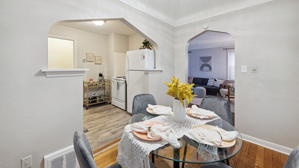 A dining area with a glass table, white tablecloth, and a vase of flowers. There are chairs around the table, and a kitchen is visible in the background. - Calming & Relaxing 2br Bungalow near UT, Tol Hosp. (Toledo)