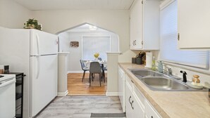 A kitchen with a white refrigerator, a sink, and a dining area with a table and chairs. - Calming & Relaxing 2br Bungalow near UT, Tol Hosp. (Toledo)