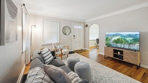 A modern living room with a sofa, ottomans, a TV, and a wooden TV stand. - Calming & Relaxing 2br Bungalow near UT, Tol Hosp. (Toledo)