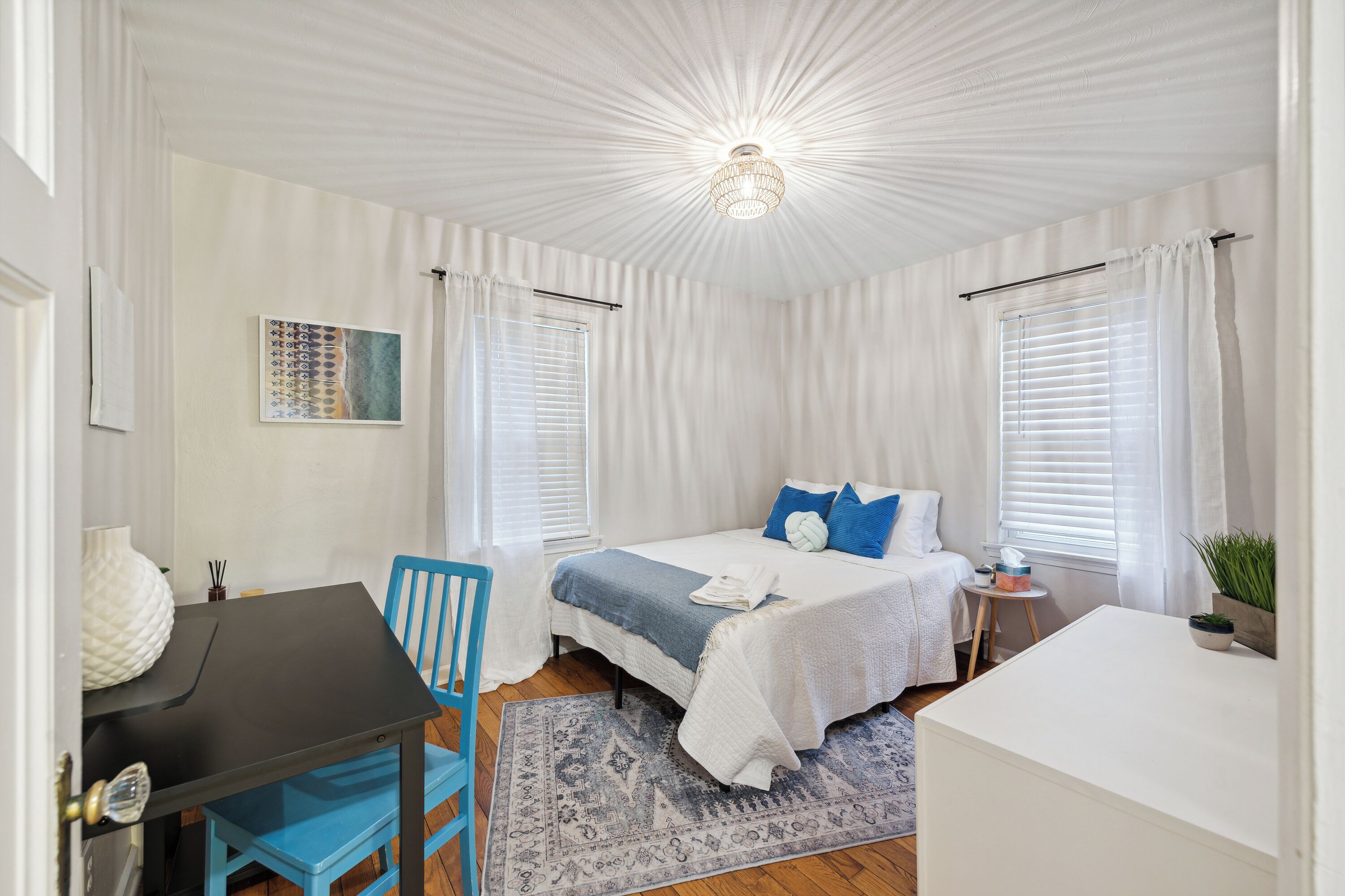 Quarto com uma cama, escrivaninha, cadeira e uma pequena mesa.