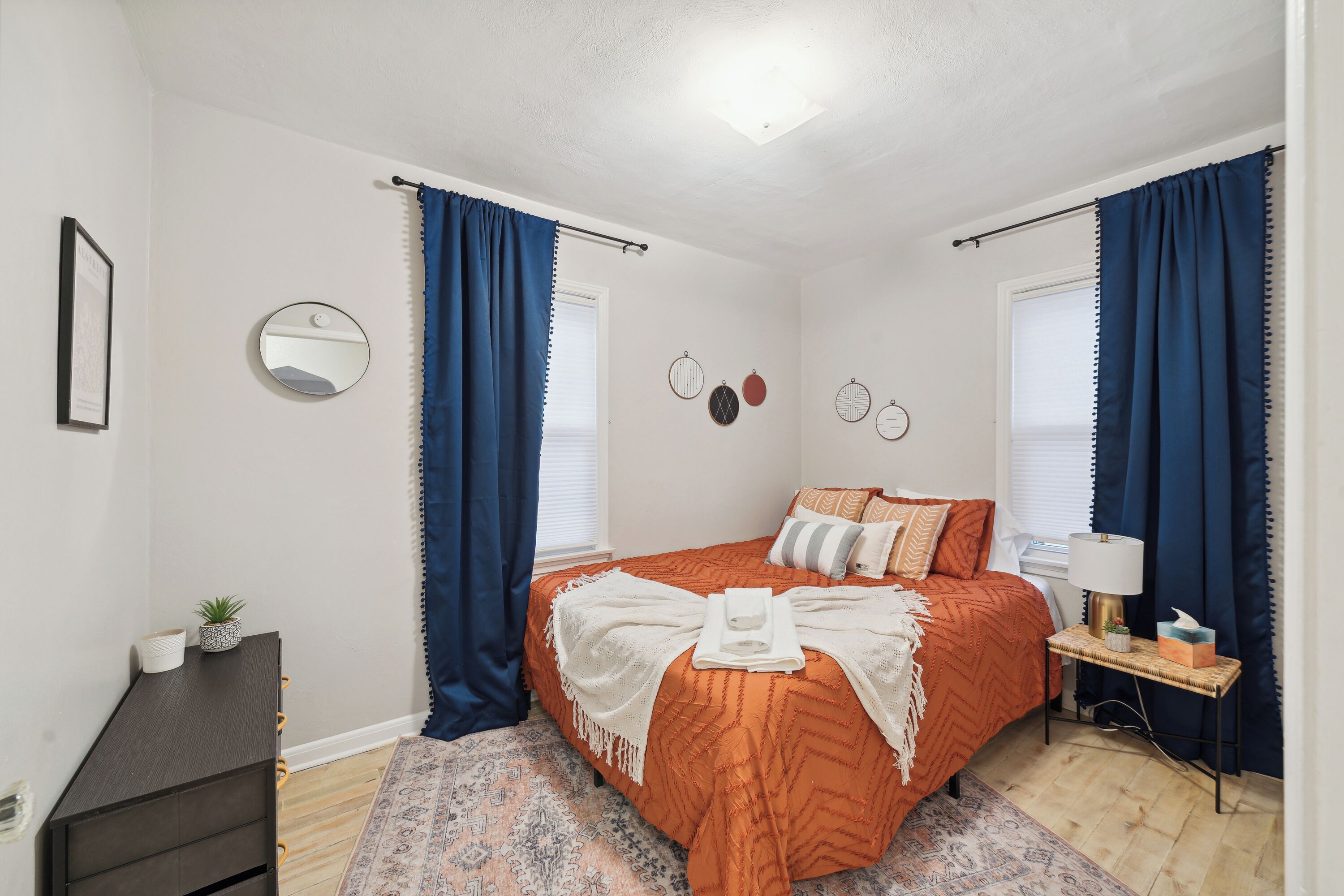 Ein Schlafzimmer mit Bett, Nachttisch mit Lampe, Kommode und Spiegel an der Wand.