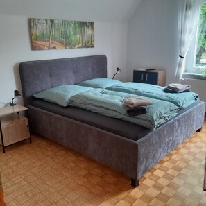 Une chambre à coucher avec un lit, une table de chevet, une armoire, un tableau et une fenêtre.