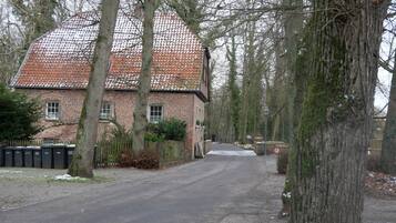 A brick building with a tiled roof, surrounded by trees and a paved road.