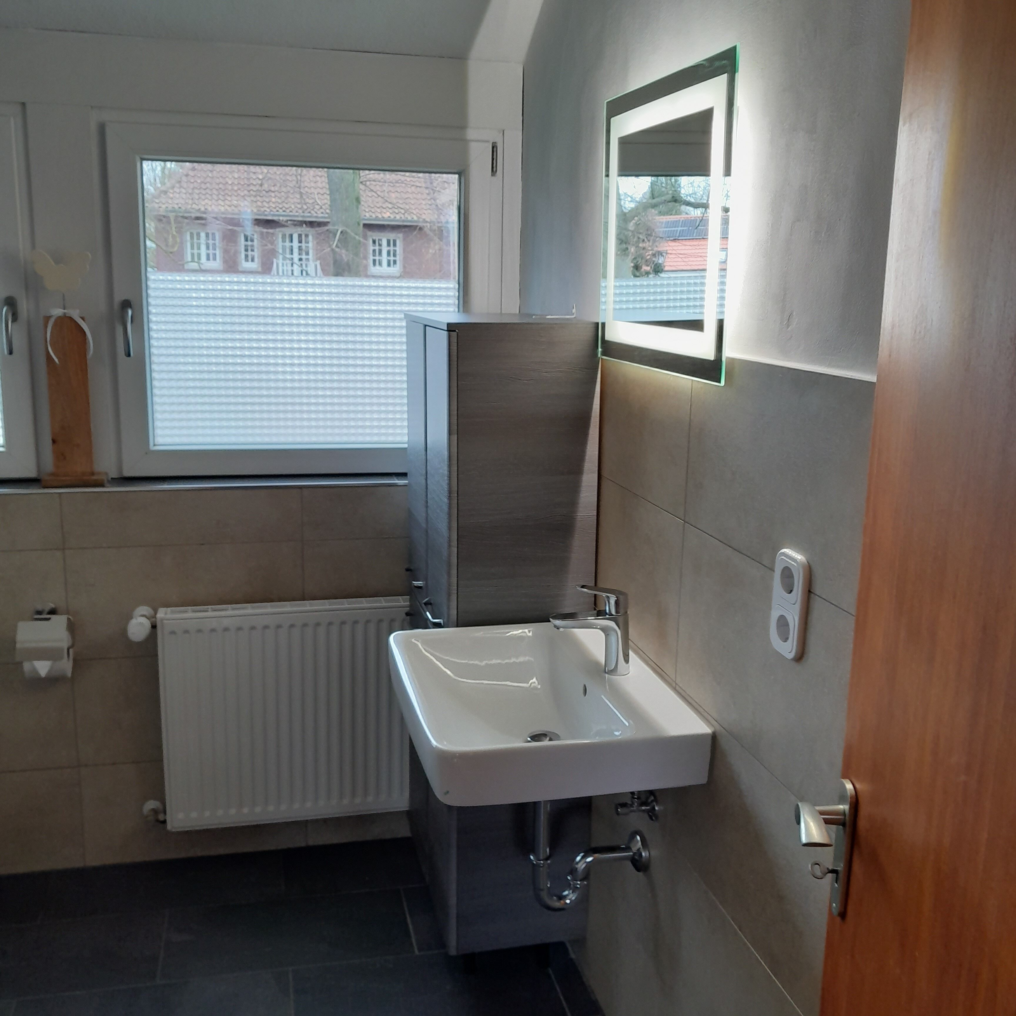 Un baño moderno con un lavamanos blanco, un espejo y una ventana.