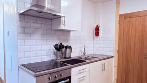 A modern kitchen with white cabinets, a stainless steel range hood, a built-in oven, and a wooden door. - Stylish Stay Near Gateacre – South Liverpool (Liverpool)